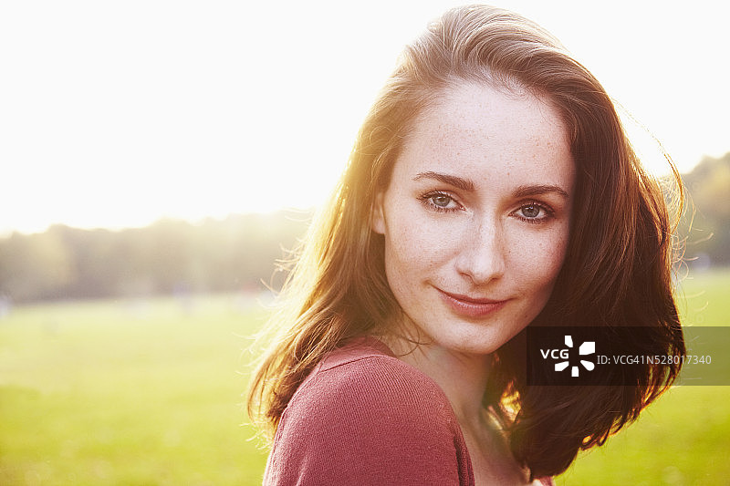一个年轻的成年女子站在日落的田野上，对着镜头微笑的肖像图片素材