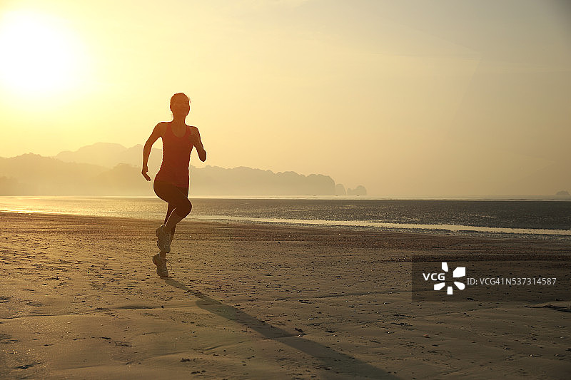 年轻女子在日出的海滩上跑步图片素材