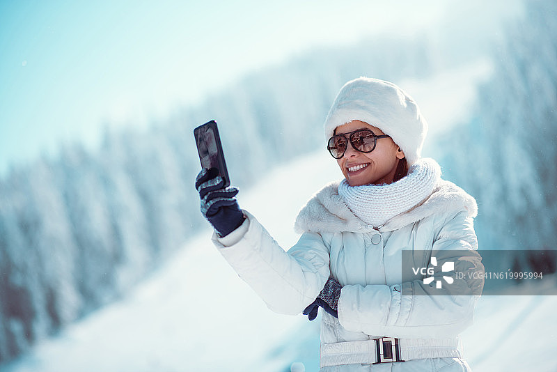 微笑的女人享受冬天，在下雪的时候自拍图片素材