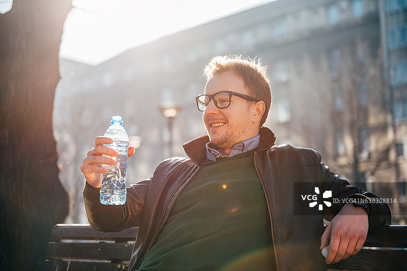 坐在公园长椅上喝水的男人图片素材