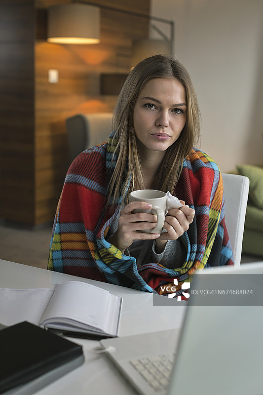 患流感的妇女端着热茶在家用笔记本电脑工作图片素材