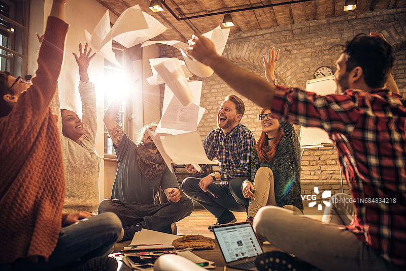 快乐的创业团队在随意的办公室里把文件扔向空中。图片素材
