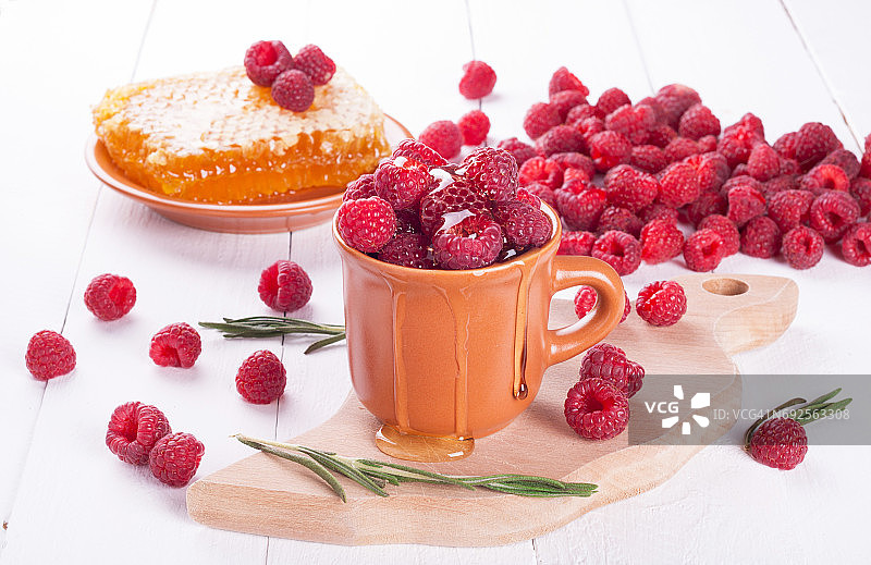 新鲜的覆盆子放在碗里，蜂蜜和迷迭香放在木背景上。夏日浆果。盘上有覆盆子和蜂窝图片素材