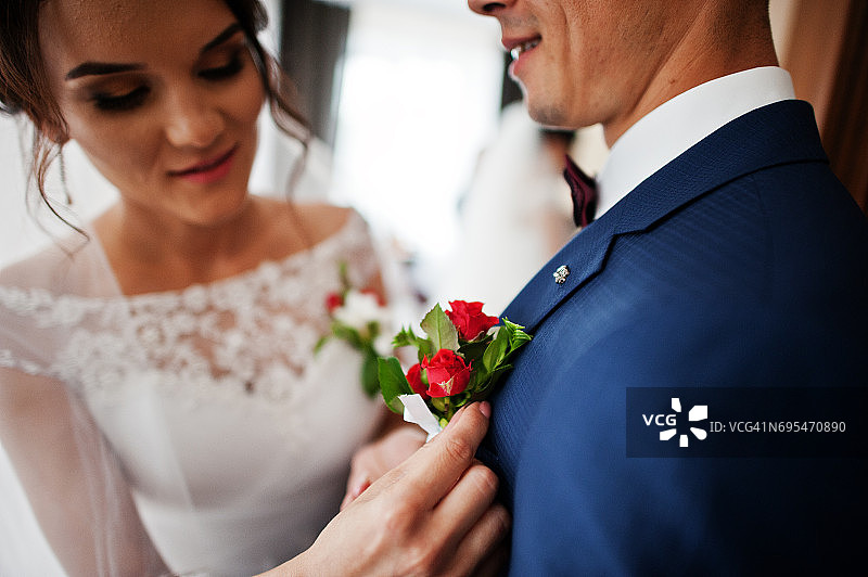 美丽的新娘在新郎的夹克上放一朵纽扣孔花。图片素材