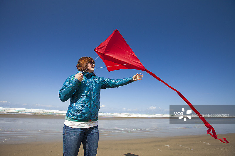 一名年轻女子在俄勒冈海岸的海滩上放飞了她的红色风筝，她伸手去拿风筝图片素材
