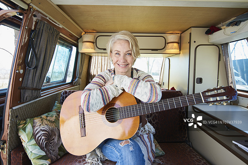 微笑的白人女人坐在露营车里拿着吉他图片素材