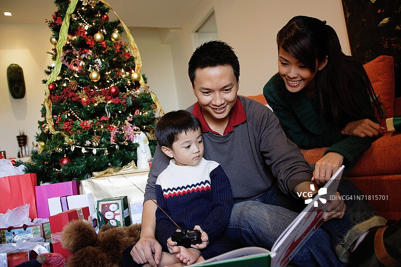 一家人带着一个孩子，在看书，身后是圣诞树图片素材