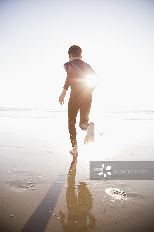 白人男孩穿着潜水服在阳光沙滩上跑步图片素材