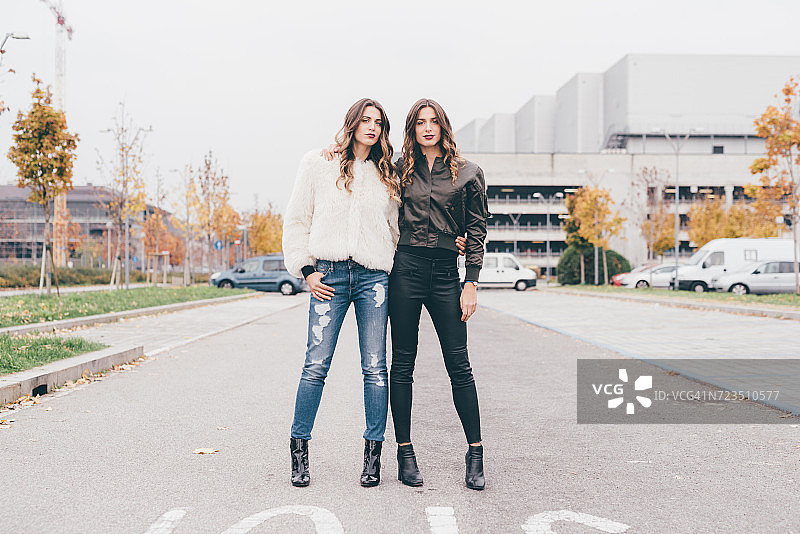 一对双胞胎姐妹的肖像，在市区，肩并肩站着图片素材