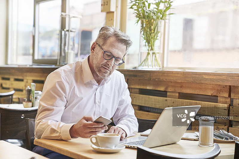 成熟的商人在咖啡馆使用笔记本电脑和手机图片素材
