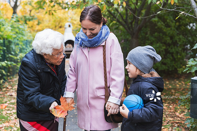 年长妇女抱着秋叶，与曾孙和女儿在公园交谈图片素材
