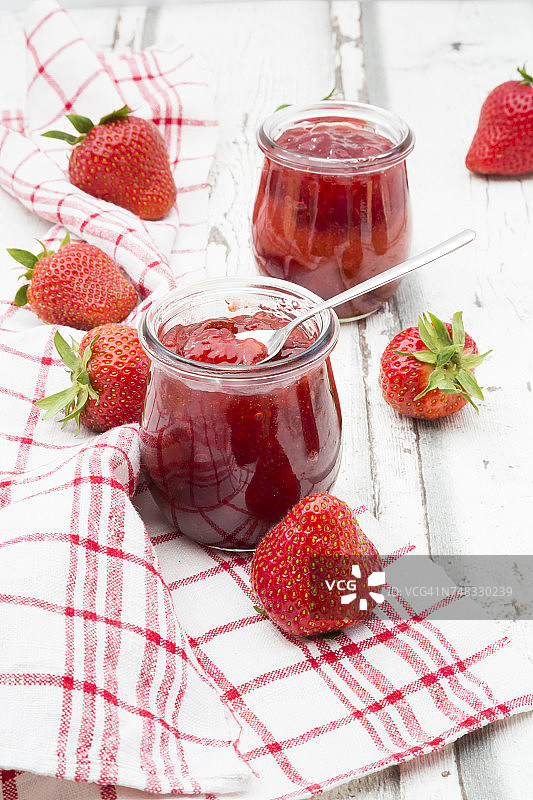 两杯自制的草莓酱，厨房毛巾和白木头上的草莓图片素材