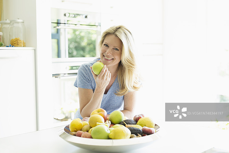 微笑的女人在家吃苹果的肖像图片素材