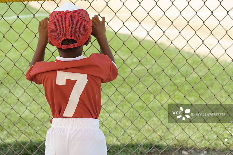 穿棒球服的男孩透过栅栏看的背影图片素材
