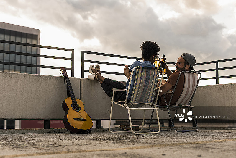 一对年轻夫妇拿着啤酒和吉他坐在屋顶上图片素材
