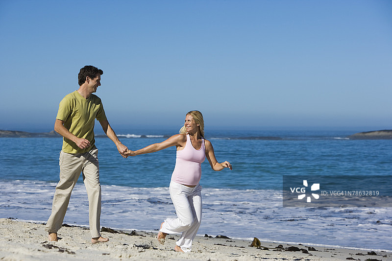 一对怀孕的夫妇走在海滩上图片素材