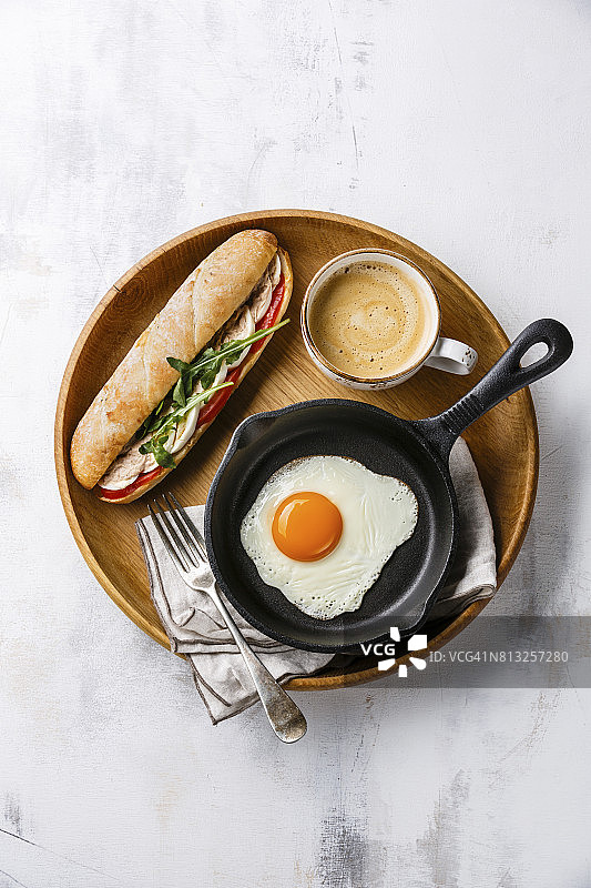 早餐有金枪鱼三明治和鸡蛋，煎鸡蛋在铁锅里，咖啡在木托盘上在白色的背景图片素材