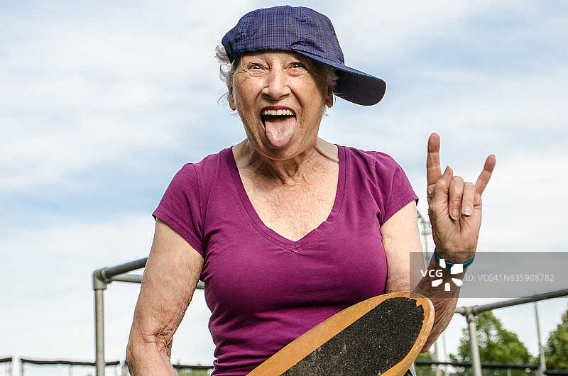 年长的女人，一边戴着棒球帽，一边拿着滑板，同时在一个夏天做一个脸和喇叭标志图片素材