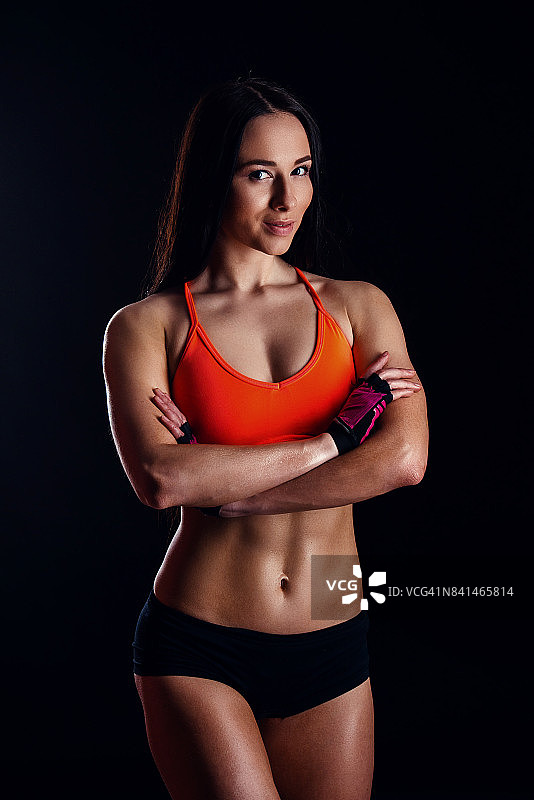 漂亮性感的健身女人显示腹部肌肉孤立在黑色背景。女性身体训练。图片素材