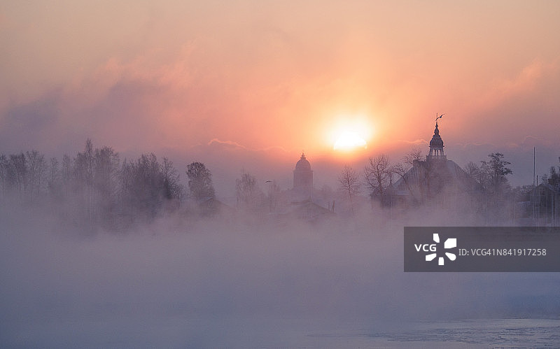 在赫尔辛基一个寒冷的冬日早晨:太阳从从冰冻的海面升起的薄雾后面升起图片素材
