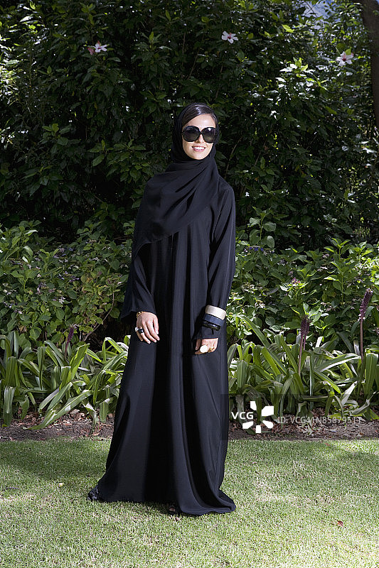 阿拉伯女人戴着墨镜站在公园里。图片素材