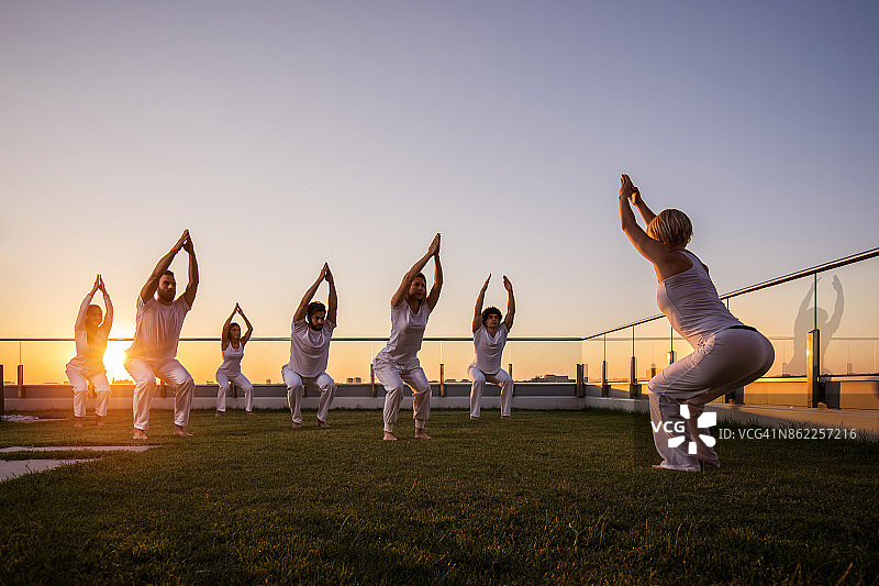 日落时分，一大群运动员在阳台上做瑜伽伸展运动。图片素材