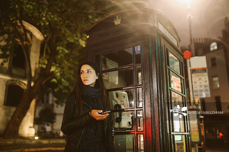 一名年轻女子在晚上走在伦敦的街道上发短信图片素材