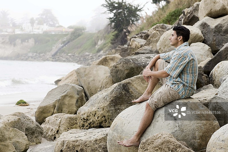 一名男子坐在加利福尼亚圣克鲁斯的岩石海岸上图片素材