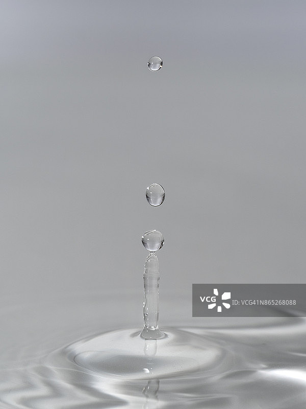 一组水滴悬在空中，落在水面上，形成图形和抽象的形式，在灰色的背景图片素材