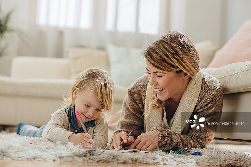 快乐的妈妈和她的小儿子在家里的地毯上涂色。图片素材