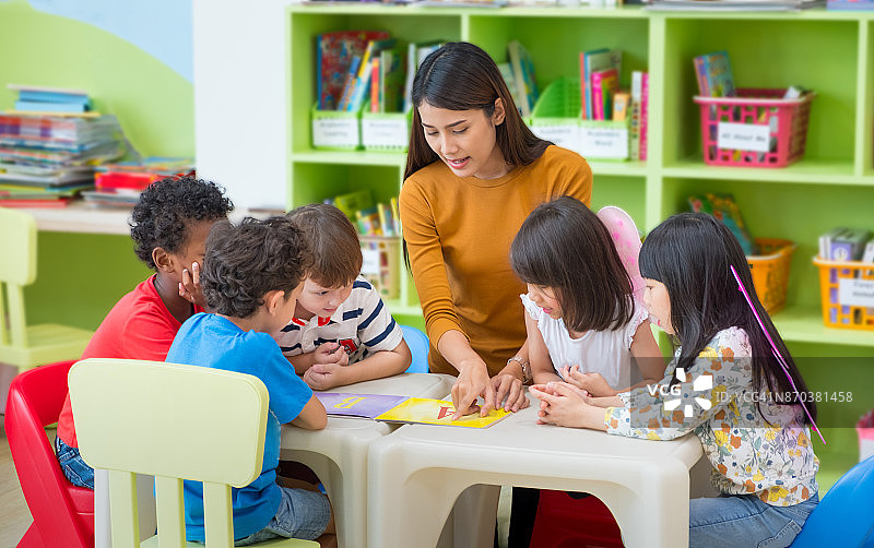 亚洲女教师教混血儿在教室看书，幼儿园的学前概念。图片素材