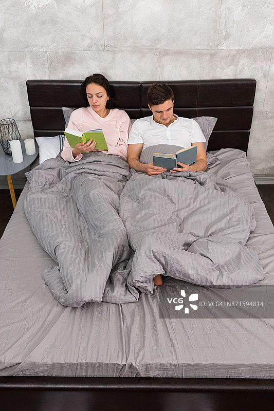 年轻迷人的一对穿着睡衣躺在床上看书图片素材