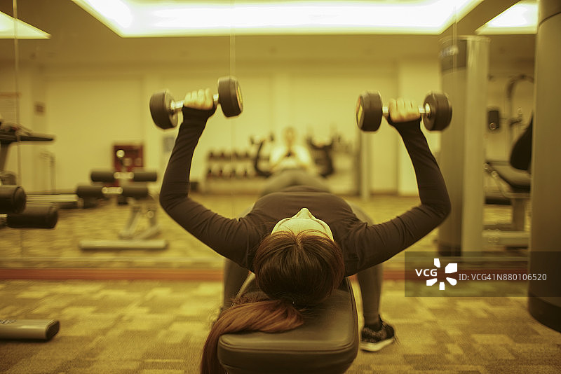亚洲女人在健身室用哑铃鼓起肌肉图片素材