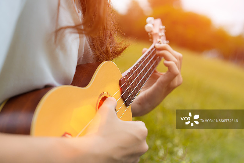 女孩在花园里弹奏尤克里里与原声吉他的特写，年轻女子演奏音乐的生活方式经典图片素材