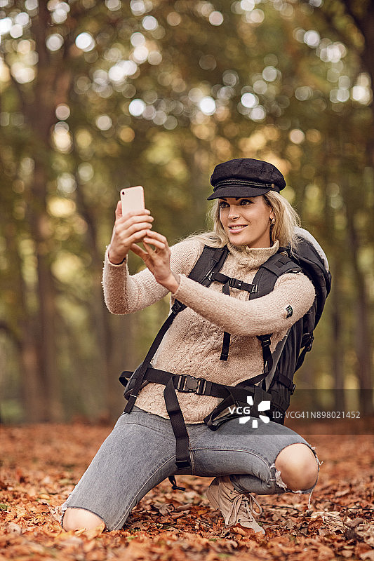 美丽年轻的金发女旅行者在秋天的欧洲乡村设置在智能手机自拍图片素材
