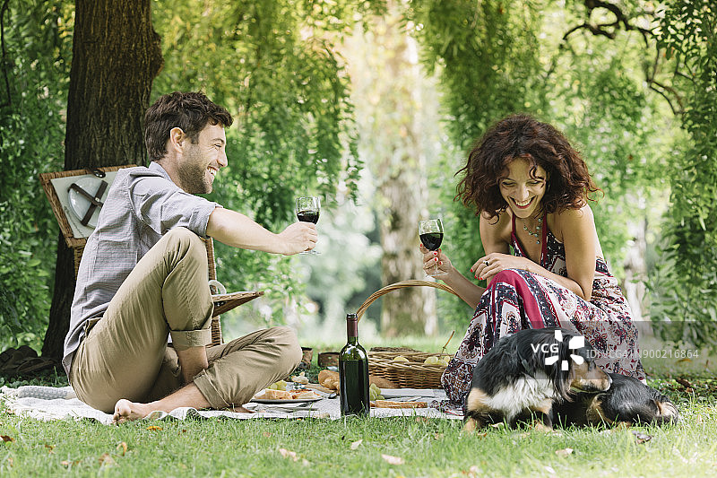 夫妇和狗在公园野餐喝红酒图片素材