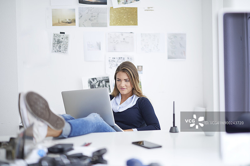 微笑的年轻女子使用笔记本电脑在办公室图片素材