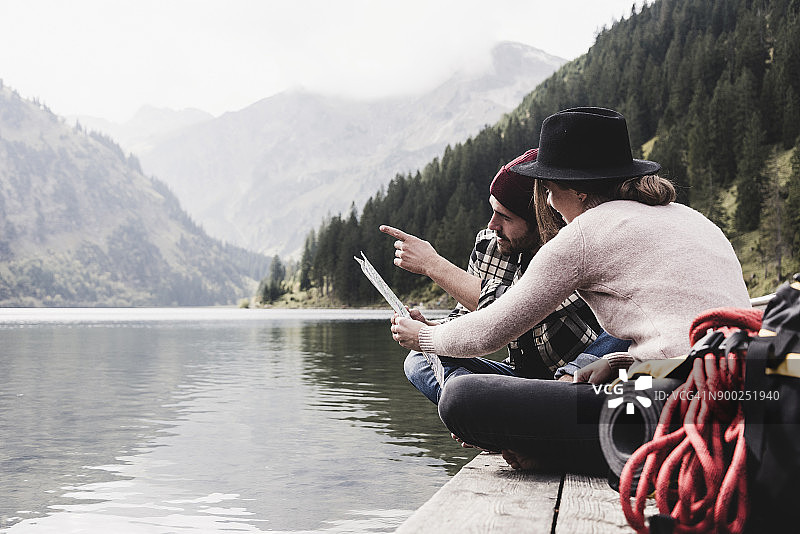 奥地利，蒂罗尔，阿尔卑斯山，夫妇与地图坐在码头上的山湖图片素材