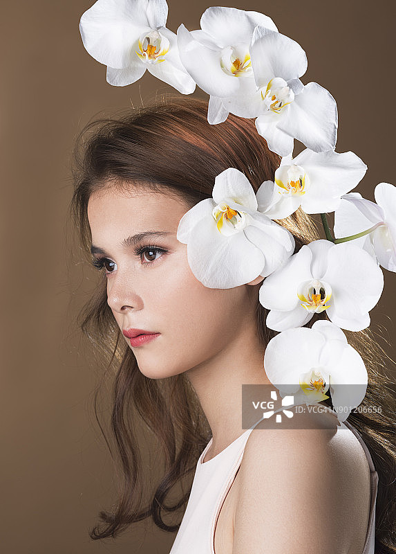 一名棕色长发的女子站在一排洁白的兰花后，目光远离镜头图片素材