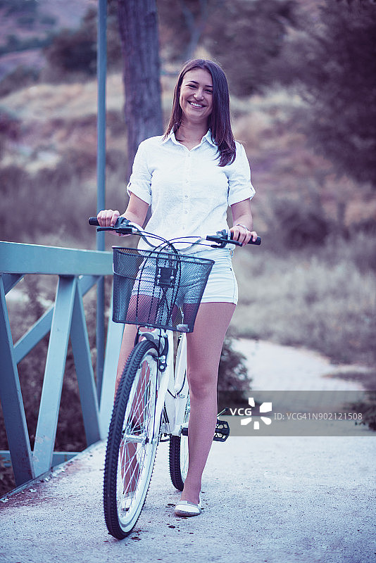 可爱的微笑年轻女性在城市公园骑自行车图片素材