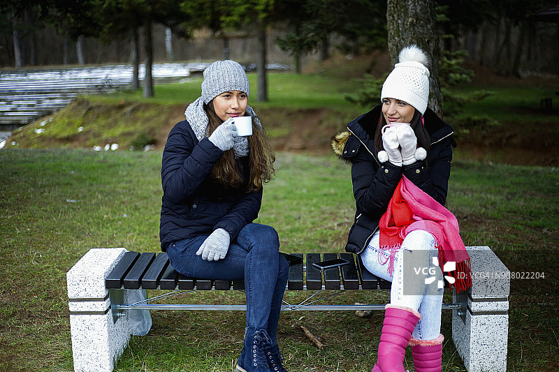 两个女性朋友在公园喝热咖啡图片素材