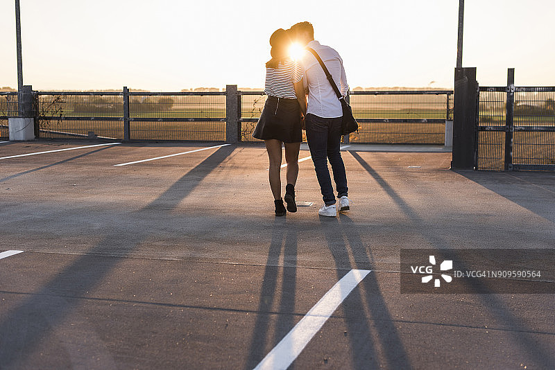 日落时分，一对年轻的情侣在停车场上接吻图片素材