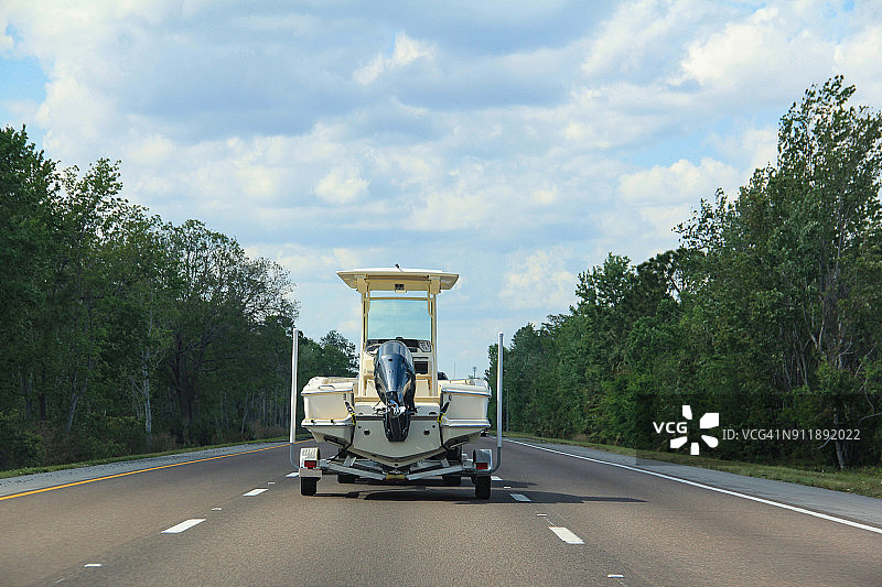 在高速公路上拖着一艘渔船拖车的车辆的后视图图片素材