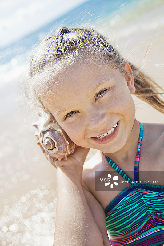 一个年轻的女孩微笑着，用她的耳朵听着贝壳的声音图片素材