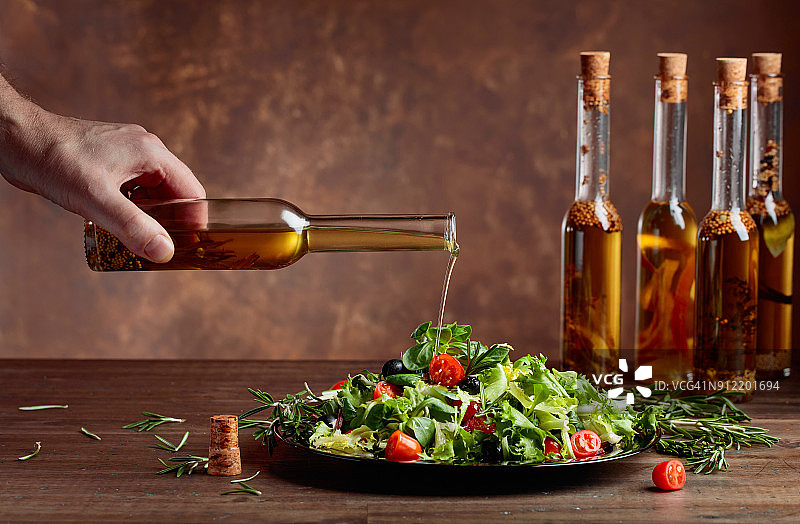 绿色沙拉和橄榄油从一个小瓶子倒。图片素材