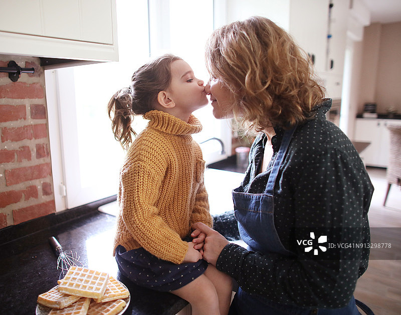 一个小女孩在厨房里亲吻她的妈妈图片素材