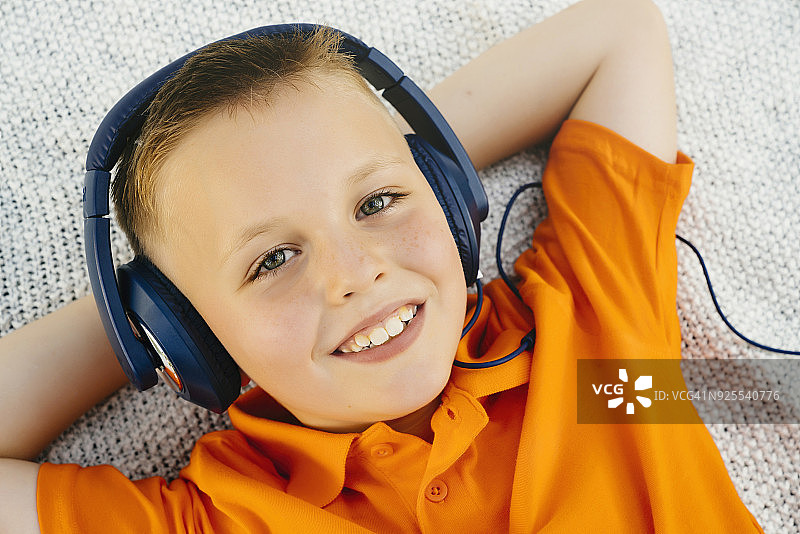 微笑的白人男孩躺在毯子上在公园听耳机图片素材