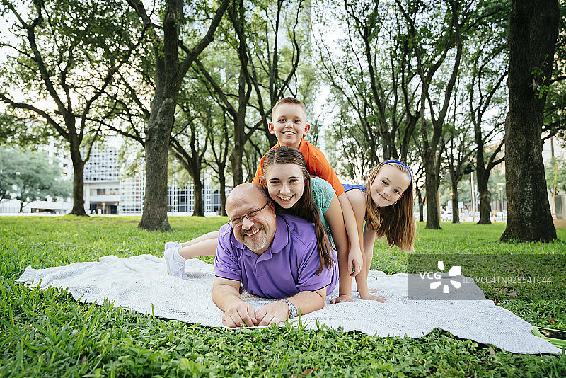 在公园里，白人男孩和女孩躺在父亲的背上图片素材