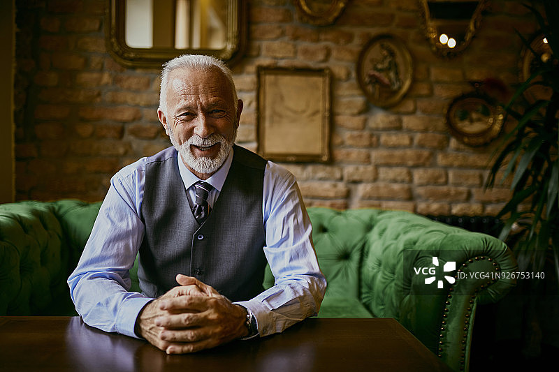 一位优雅的老人坐在咖啡馆的沙发上微笑的肖像图片素材