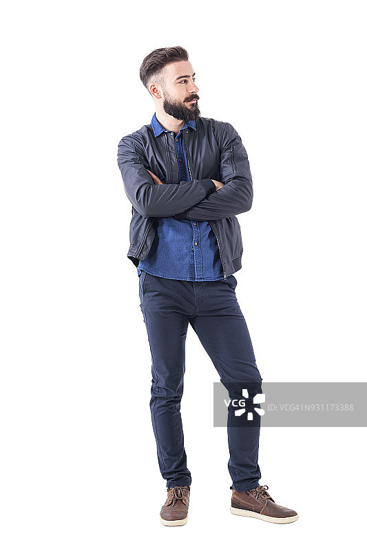 自信的年轻胡子男子，穿着短夹克交叉双臂看向别处。图片素材